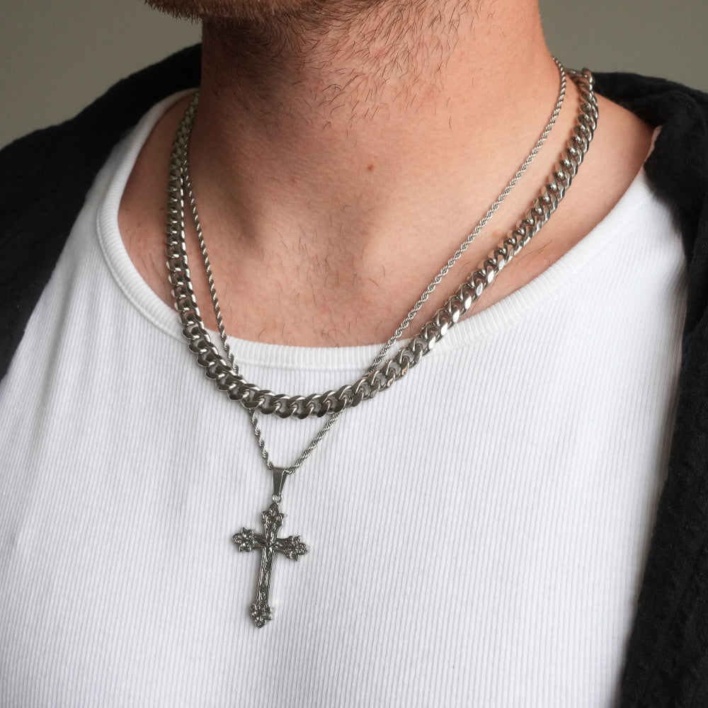 Person wearing a white shirt with a black sleeve and two silver chain necklaces, one with a cross pendant.