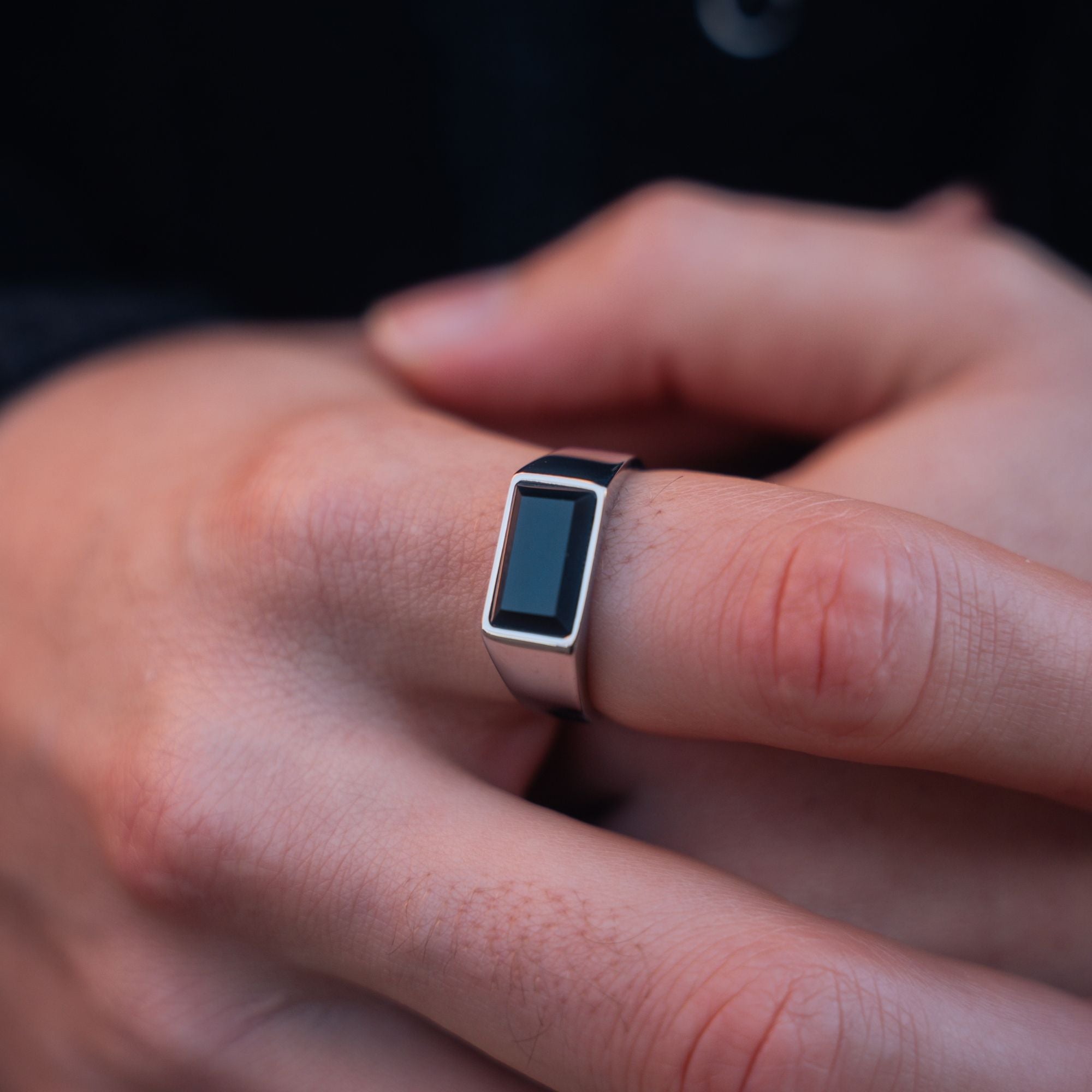 A close-up of a silver-toned ring with a rectangular black inlay, worn on a person's finger.