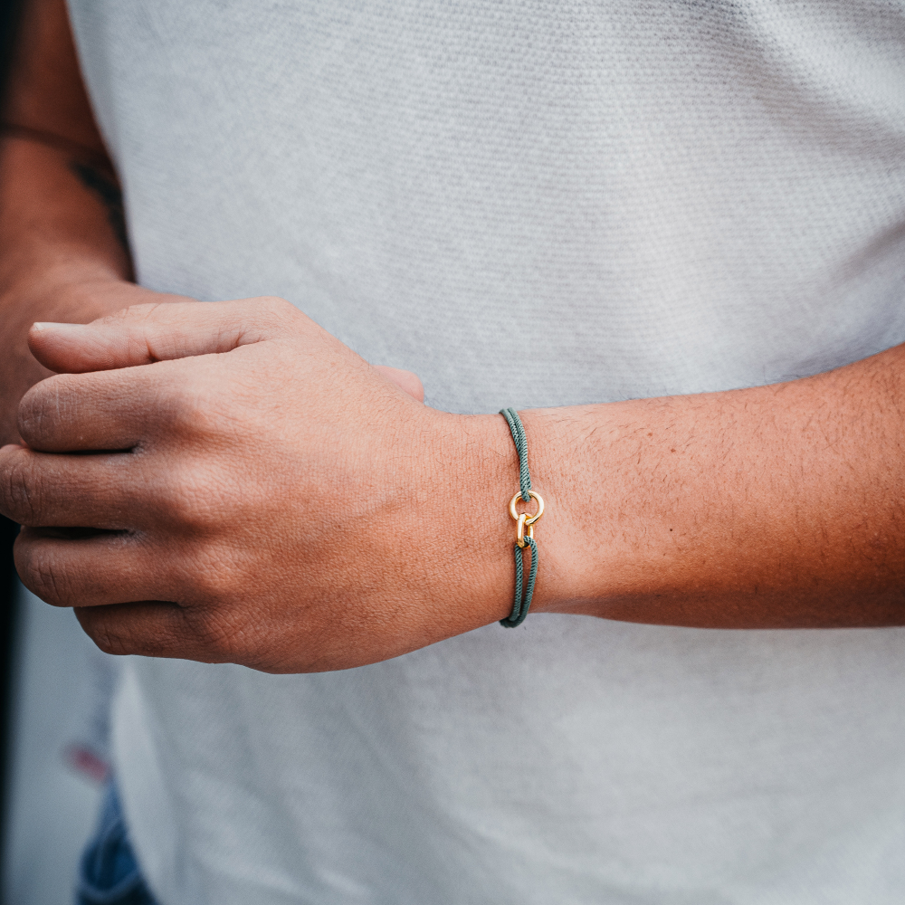 A person's wrist wearing a green nylon bracelet with gold plating, interlocked with sterling silver.