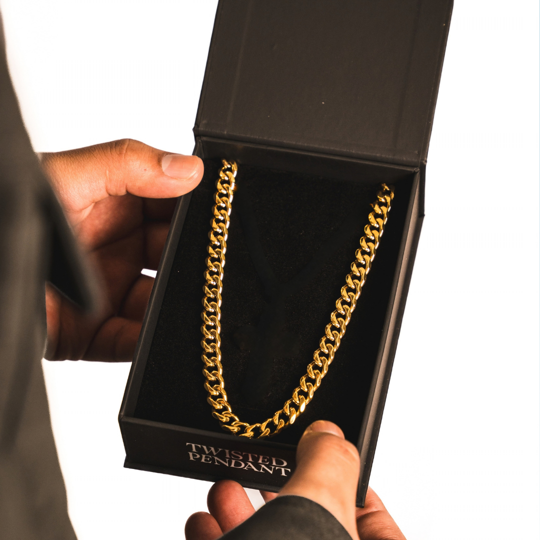 A gold-toned chain necklace displayed inside an open black jewelry box held by two hands against a white background. The box is branded TWISTED PENDANT.