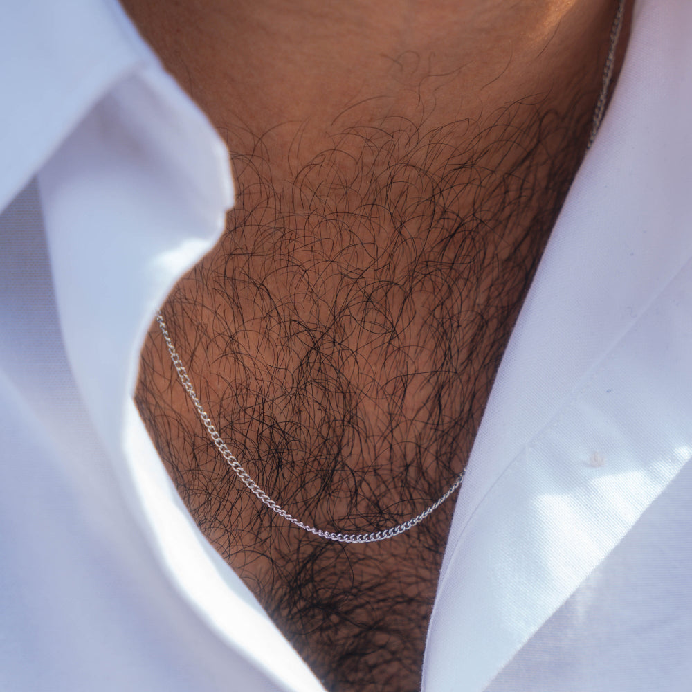Close-up of a silver chain necklace on a person wearing a white shirt.