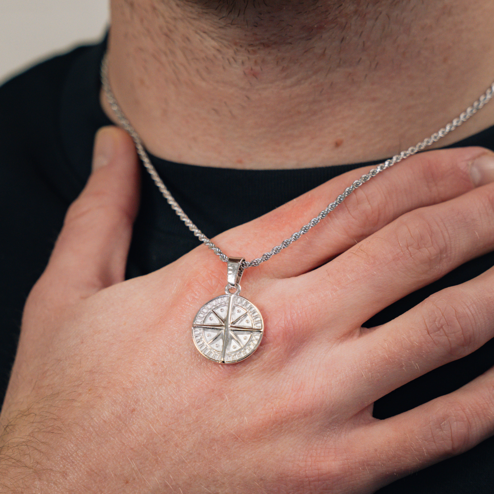 A silver compass pendant necklace with a detailed design on the pendant and a thin rope chain.