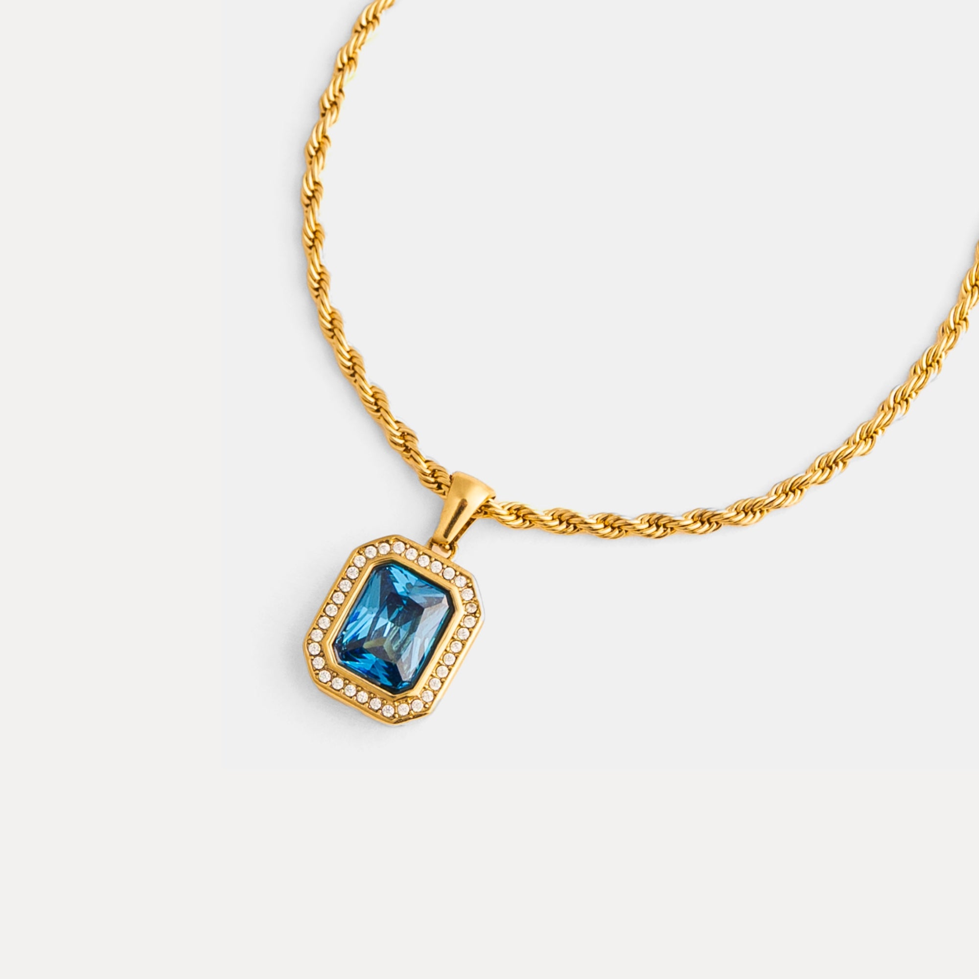 Gold necklace with a blue gemstone pendant on a white background