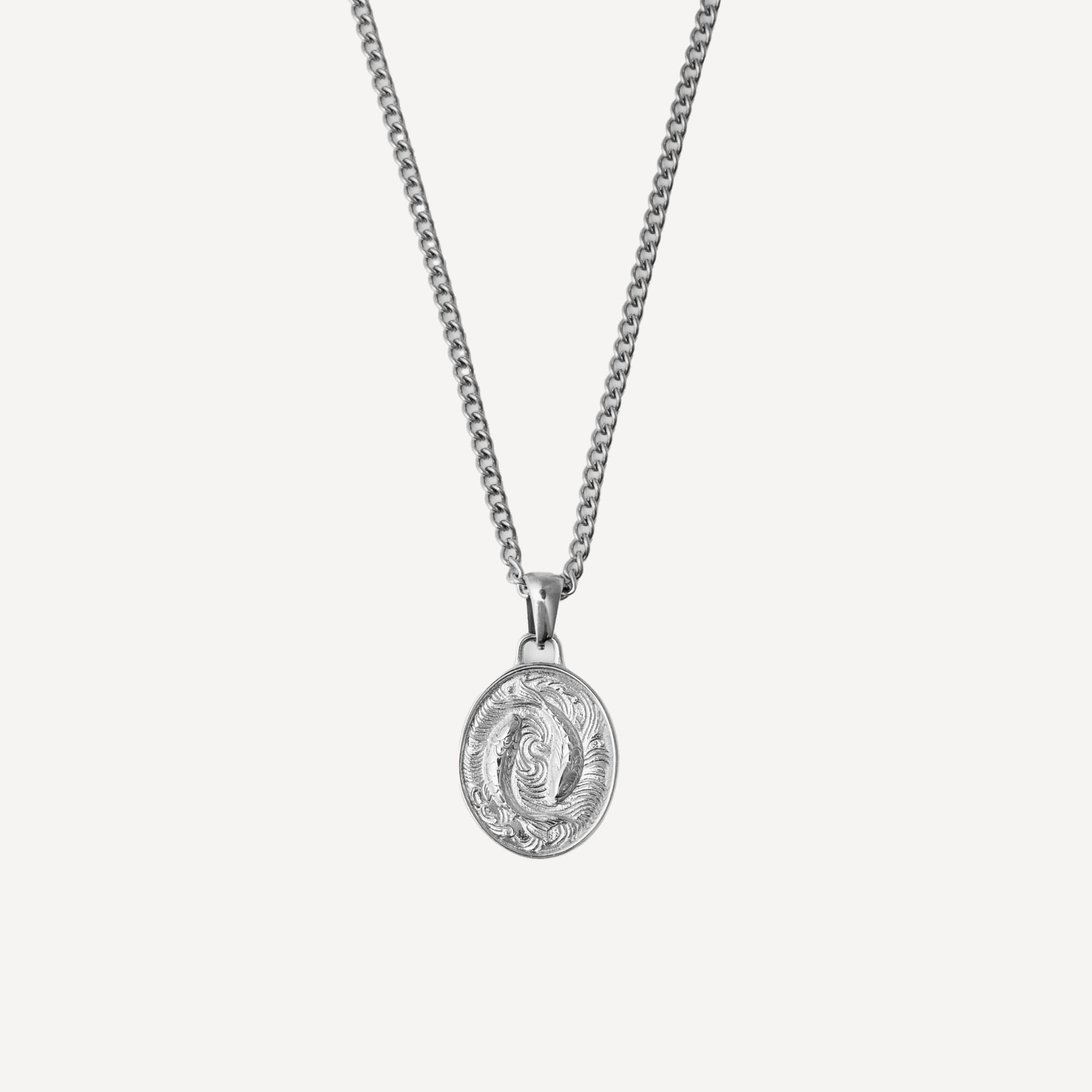 A silver chain necklace with an oval pendant featuring a detailed, embossed design, shown against a light gray background.