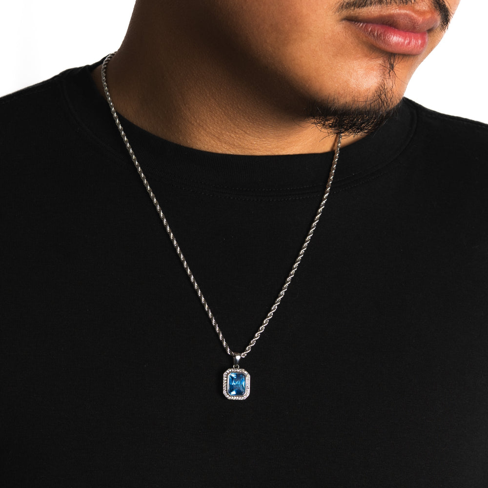 Man wearing a black shirt with a silver necklace featuring a blue gemstone pendant.