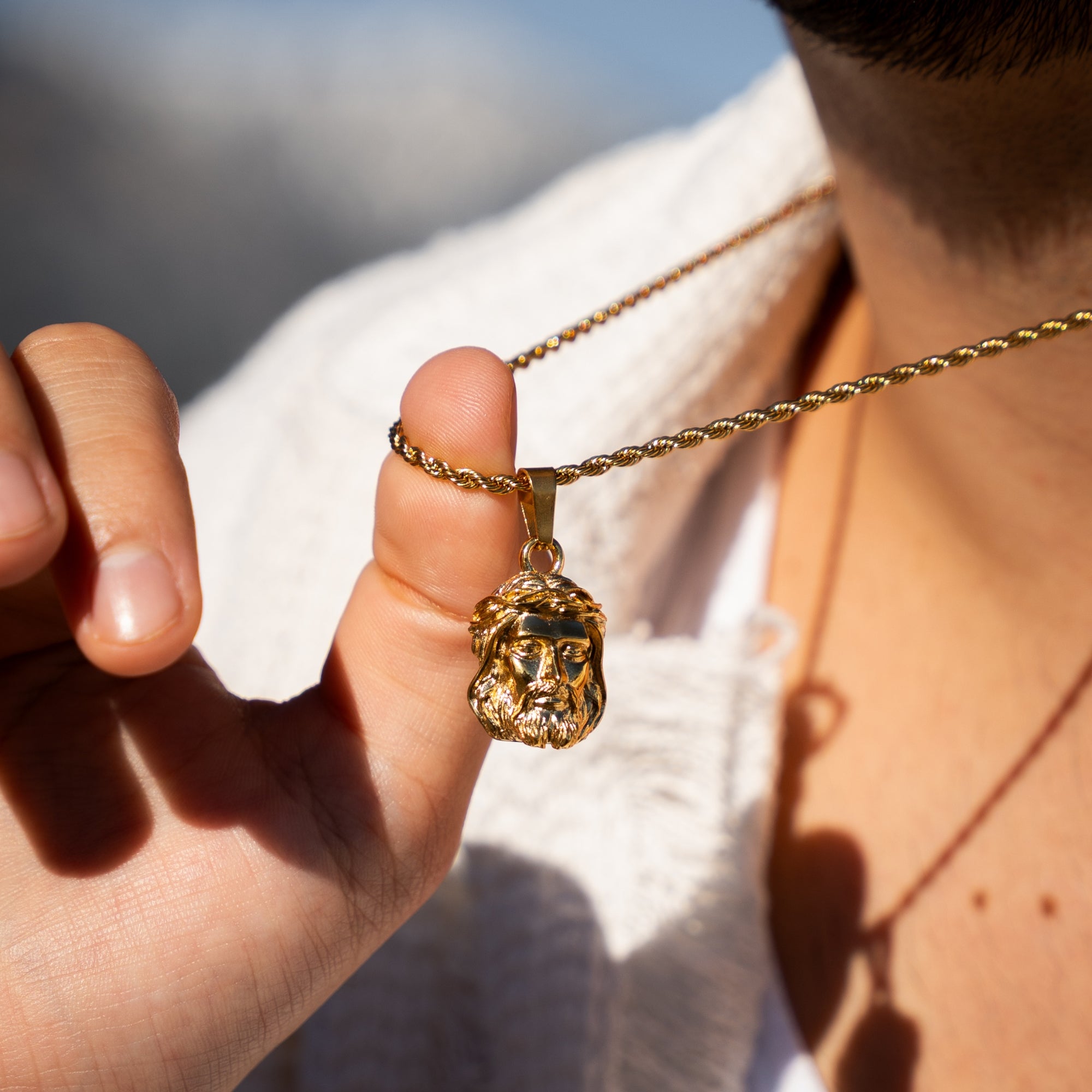 Gold necklace with a pendant featuring a face design held by a hand against a blurred background.