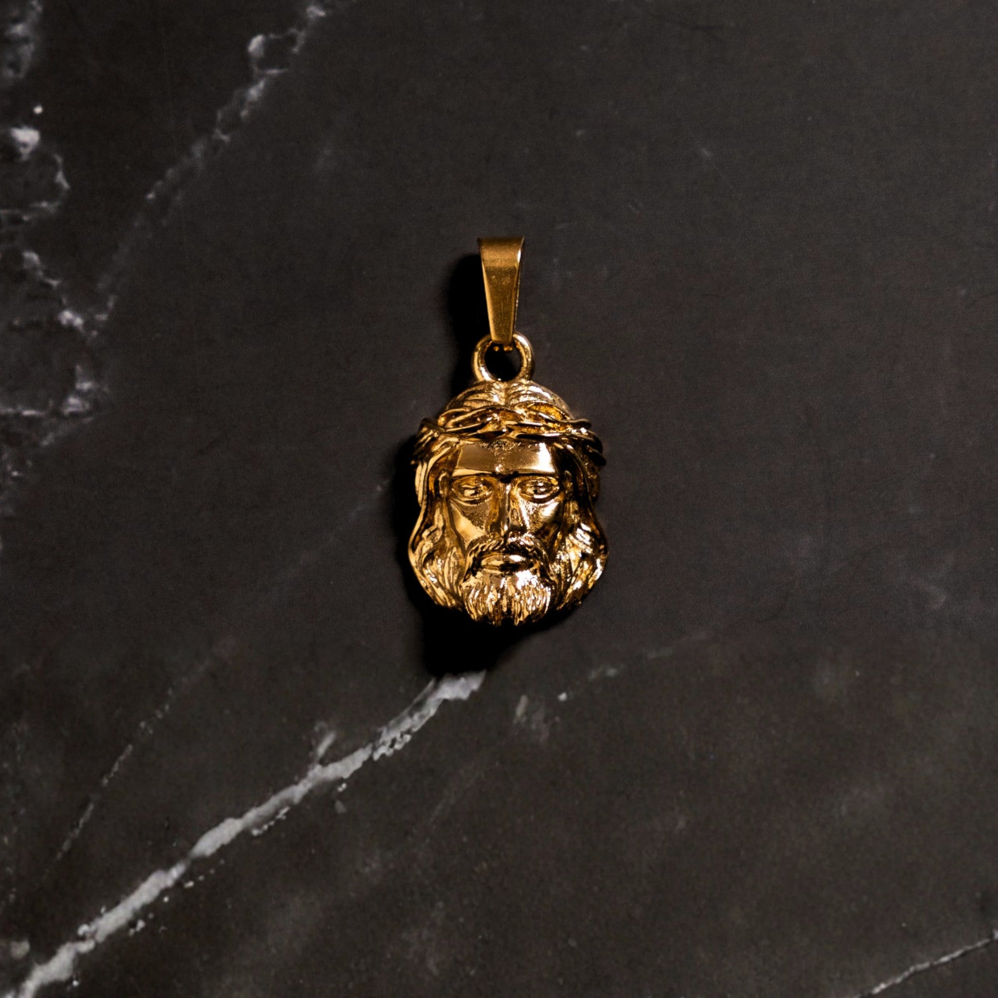 Gold pendant with a face design on a dark marble surface