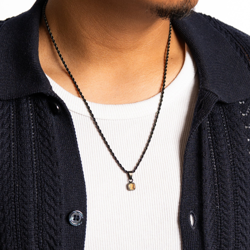 Person wearing a black chain necklace with a pendant, dressed in a dark jacket over a white shirt.