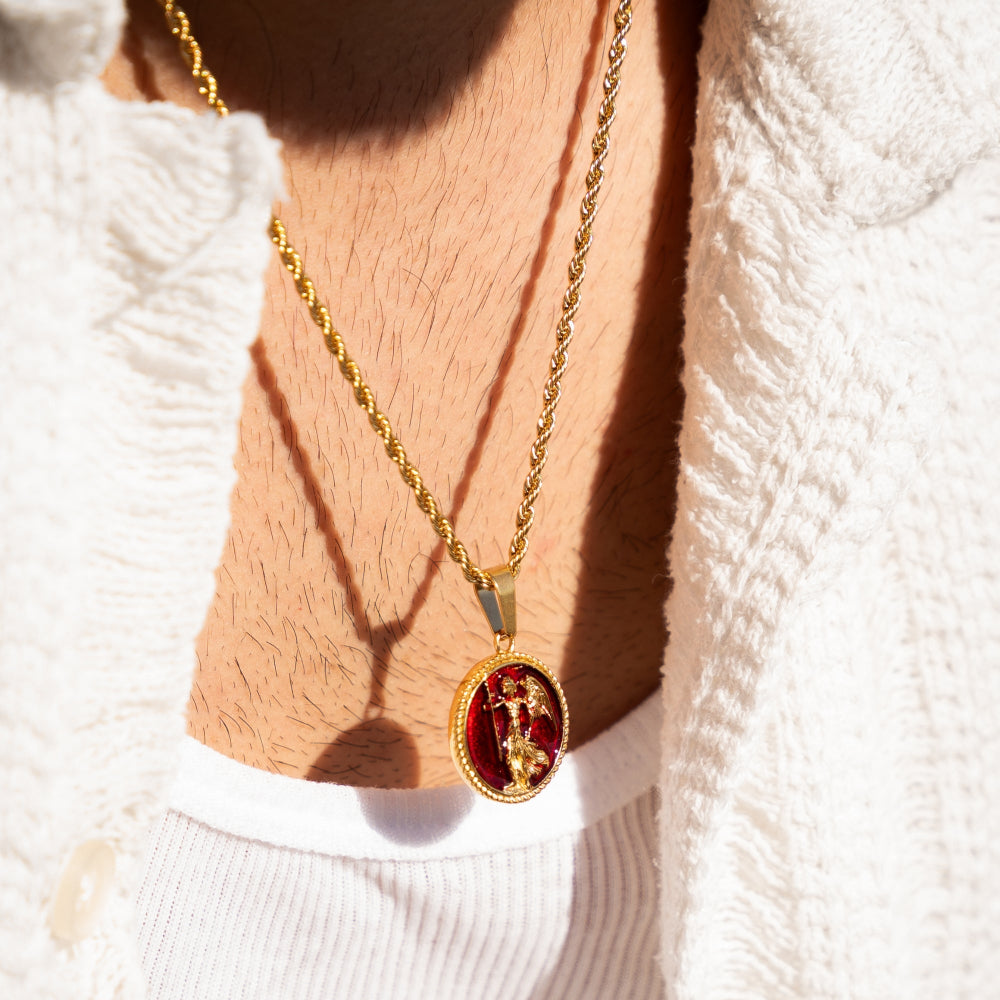 Gold necklace with a red pendant on a person wearing a white sweater.