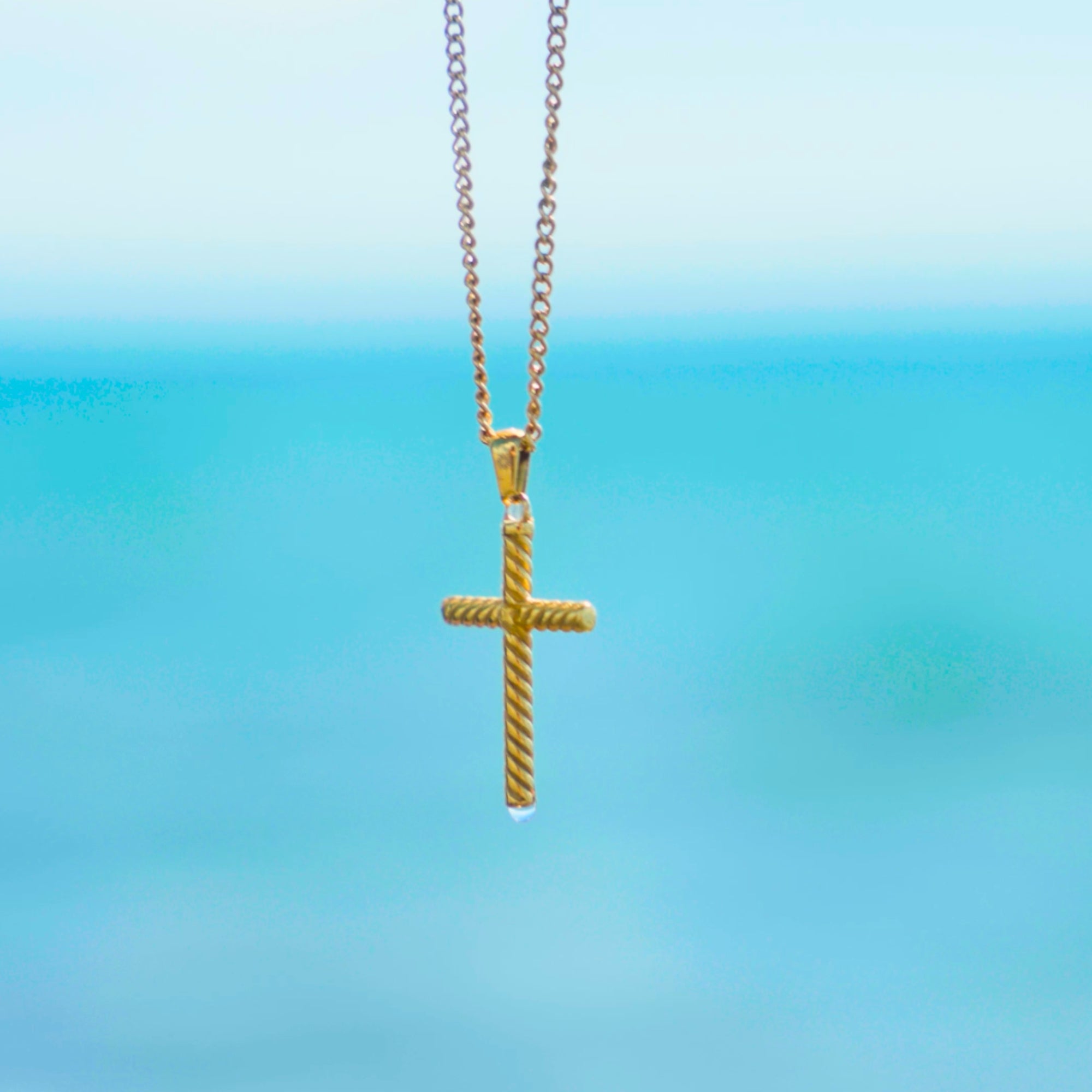 Gold cross necklace on a blue gradient background