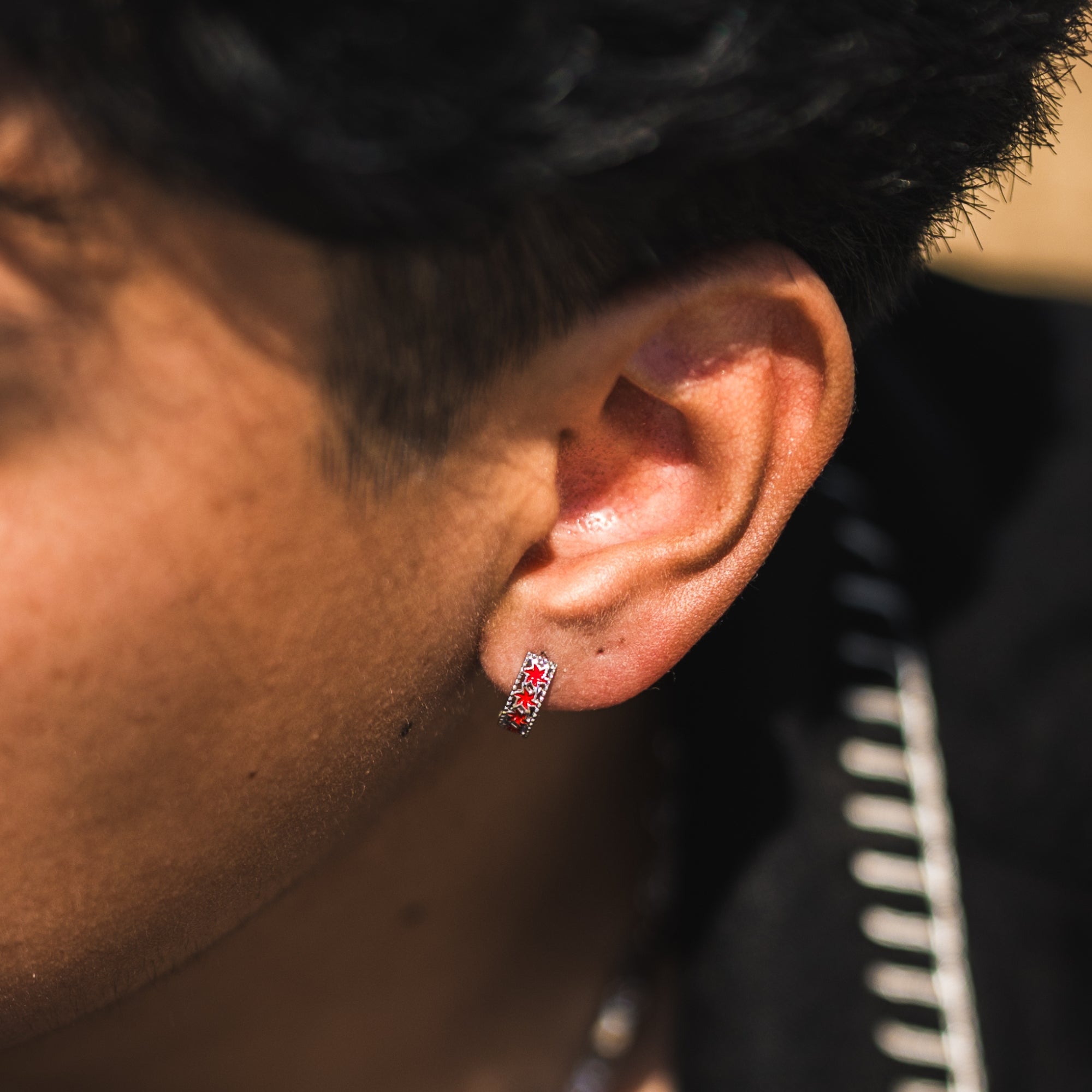 Close-up of an ear with a red and silver earring against a blurred background