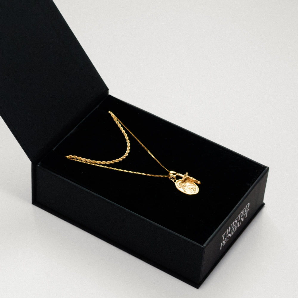 Gold necklace with a pendant in an open black jewelry box on a light gray background