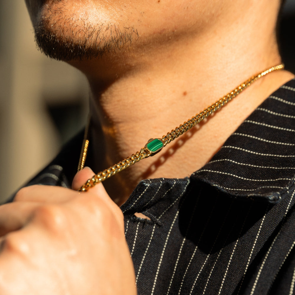 Gold chain with a green gemstone held by a person wearing a black pinstripe shirt.