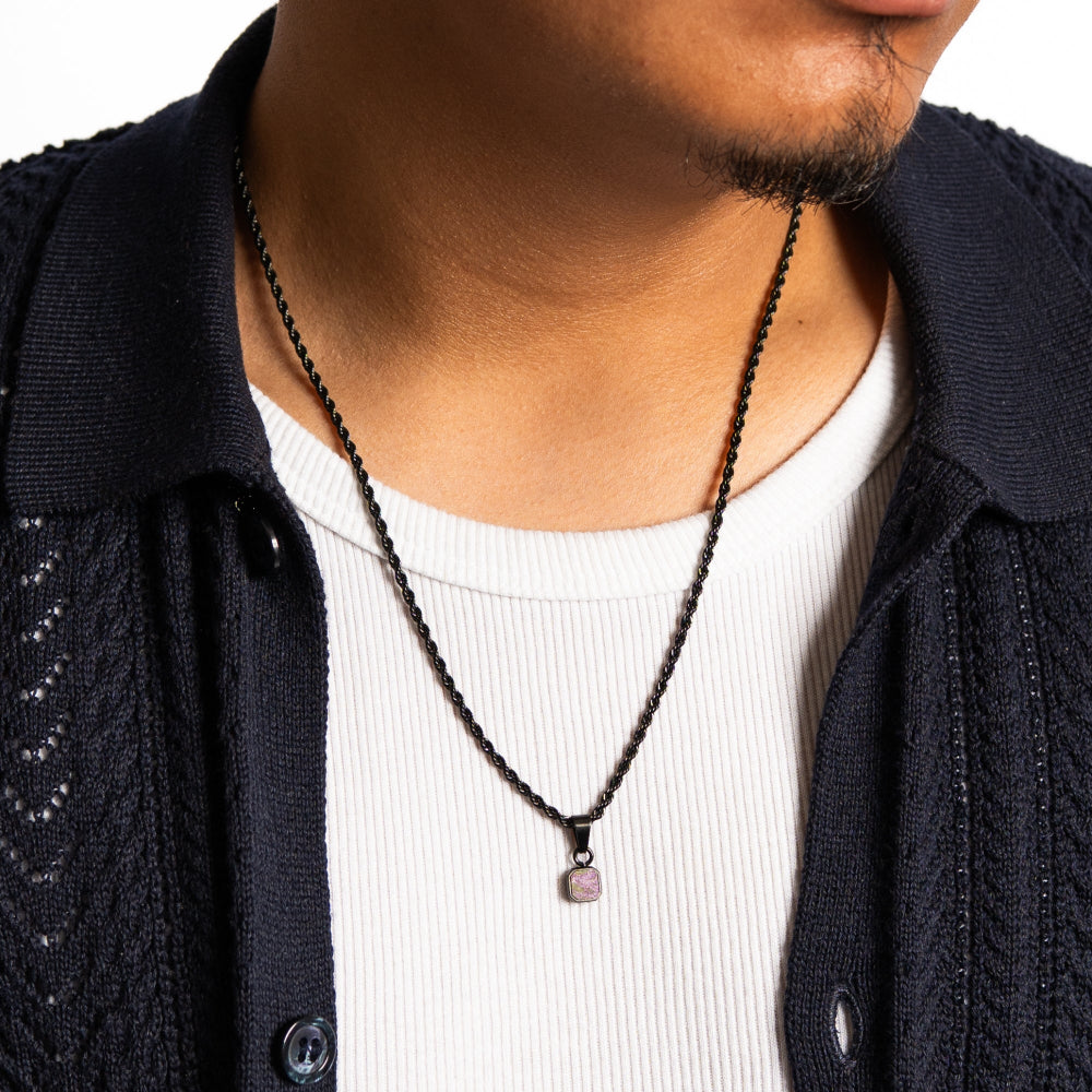 Person wearing a black beaded necklace with a pendant.
