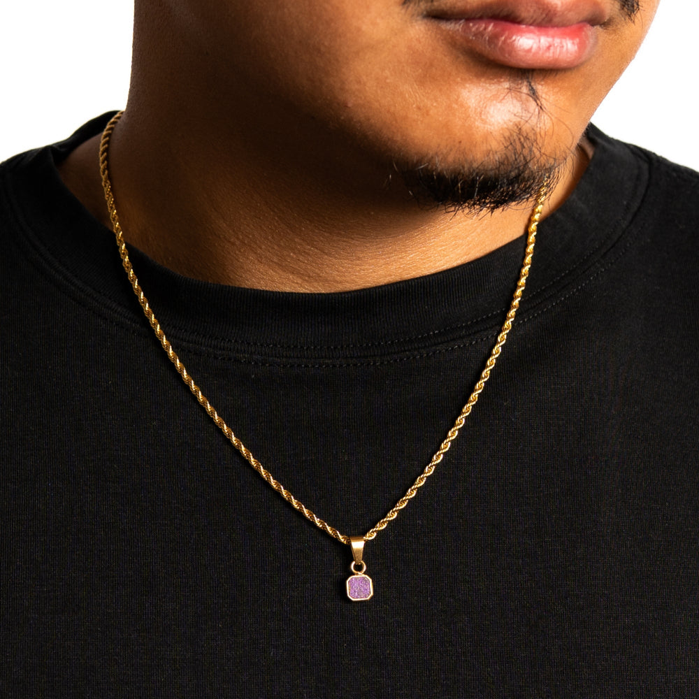 Man wearing a gold necklace with a purple pendant on a black shirt.