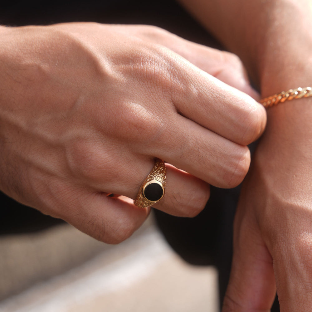 Close-up of a hand wearing a gold ring with a black stone on a blurred background