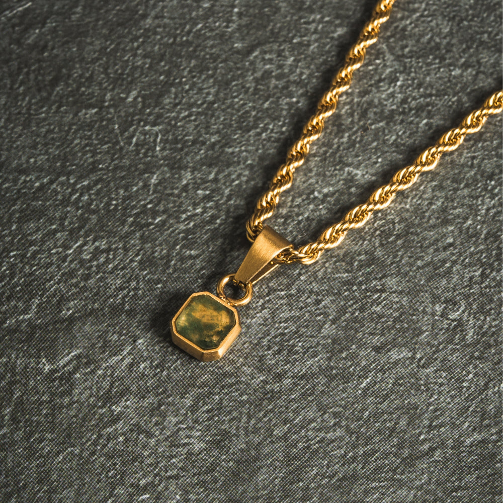 Gold necklace with a green stone pendant on a dark gray background