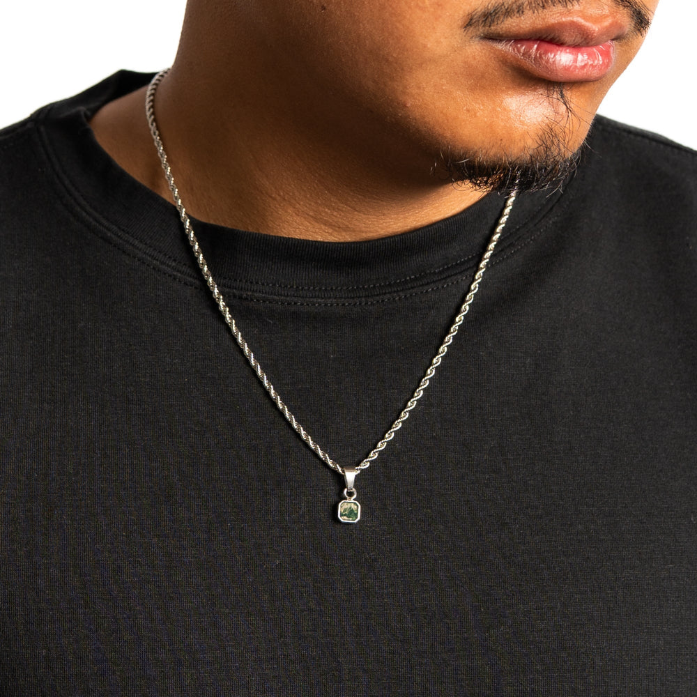 Man wearing a black shirt with a silver necklace featuring a green gemstone pendant.