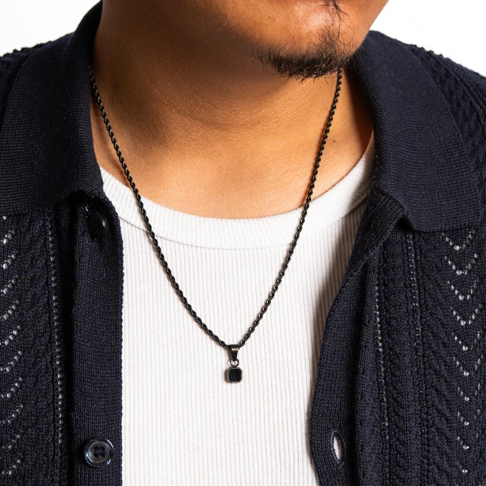 Person wearing a black chain necklace with a small pendant on a white background