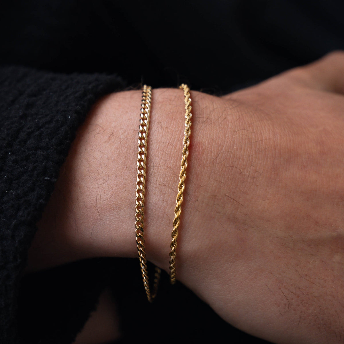 Gold chain bracelet on a wrist with a dark background