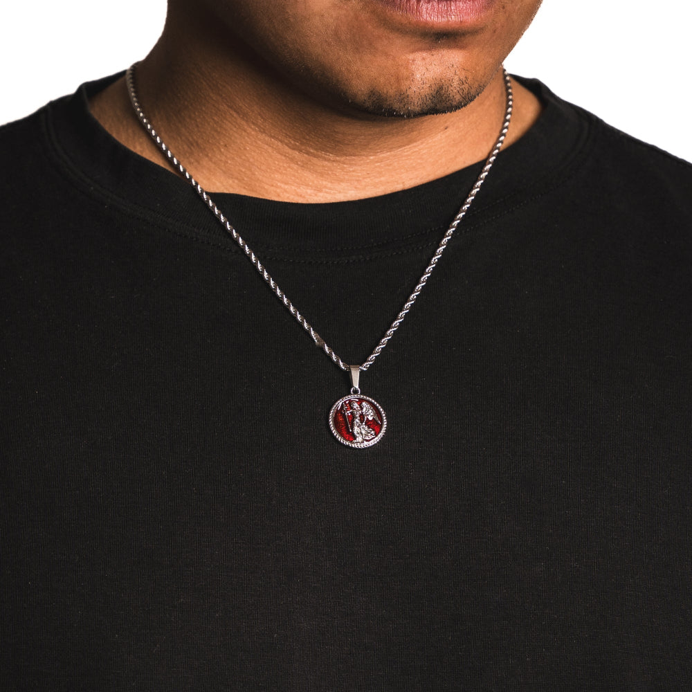 Person wearing a black shirt with a silver necklace featuring a round pendant.