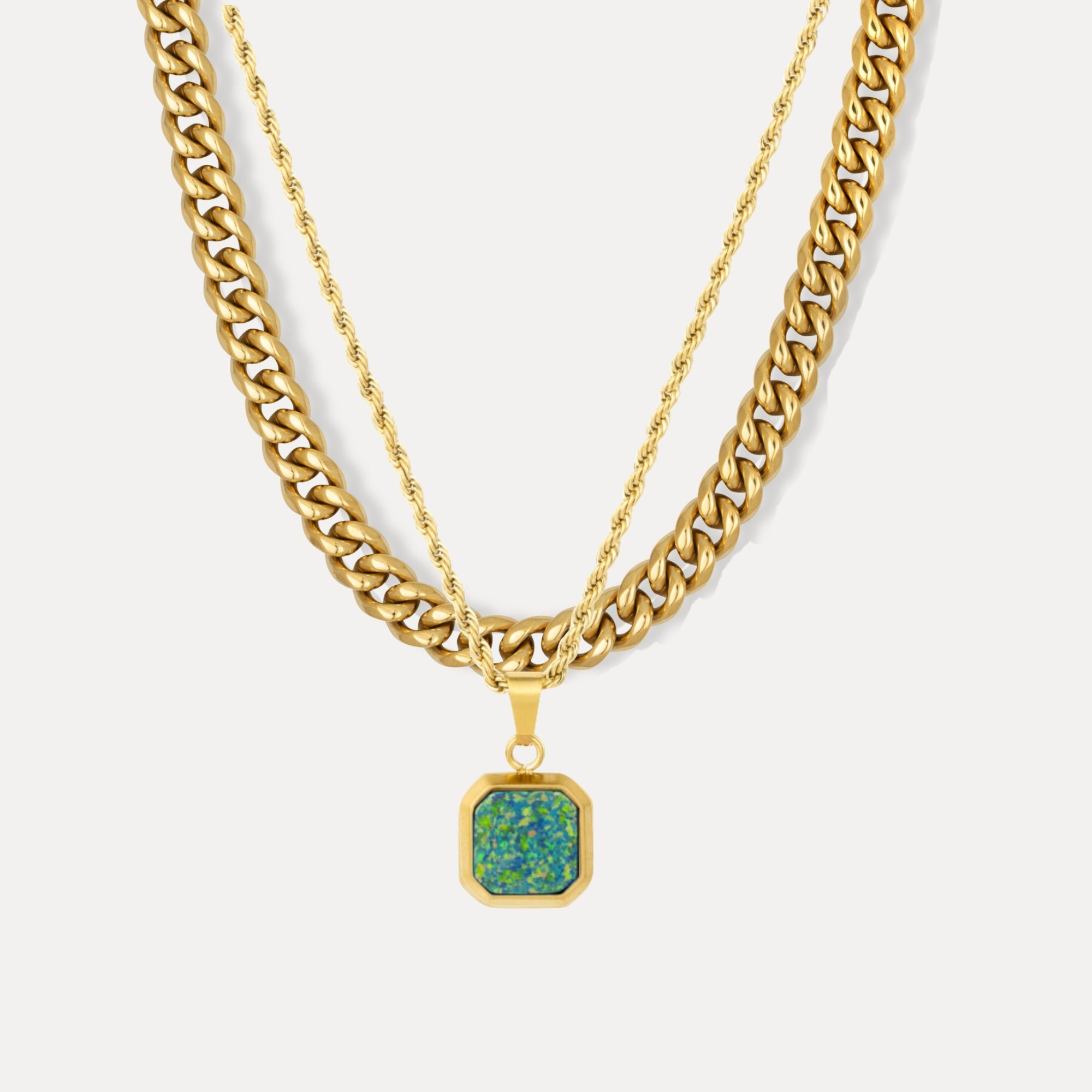 Gold chain necklace with a green pendant on a light gray background