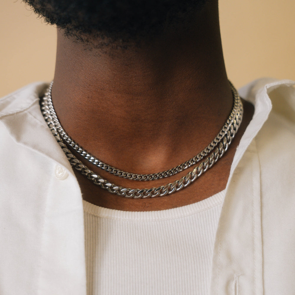 Person wearing a silver chain necklace on a beige background