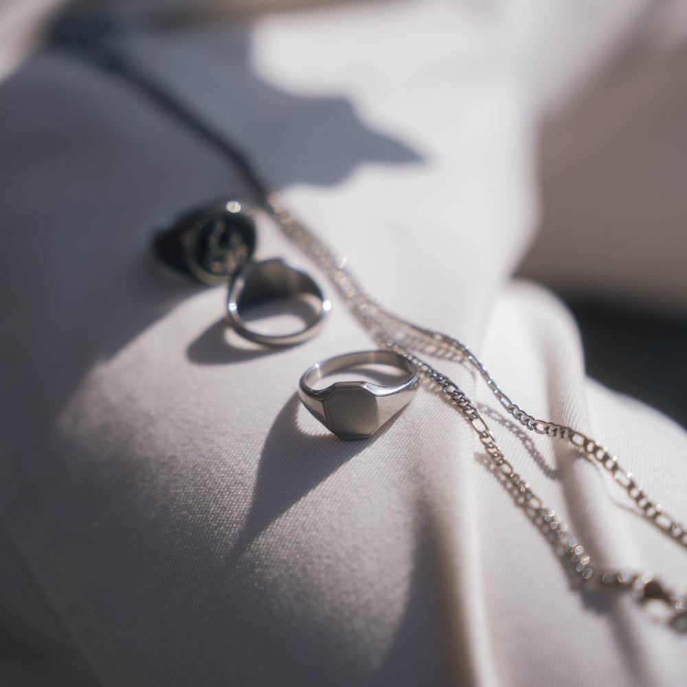Silver rings and necklace on a textured surface with soft lighting