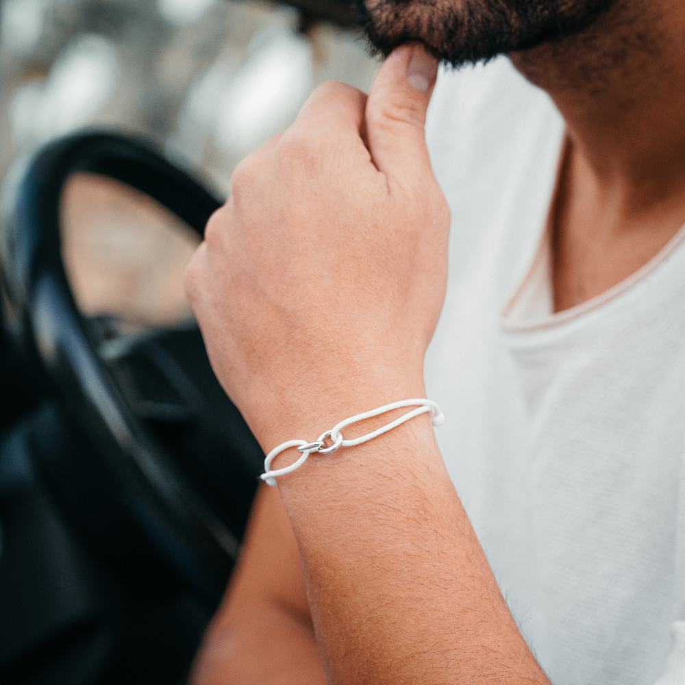 A person wearing a white drift bracelet with sterling silver accents, sitting in a vehicle.