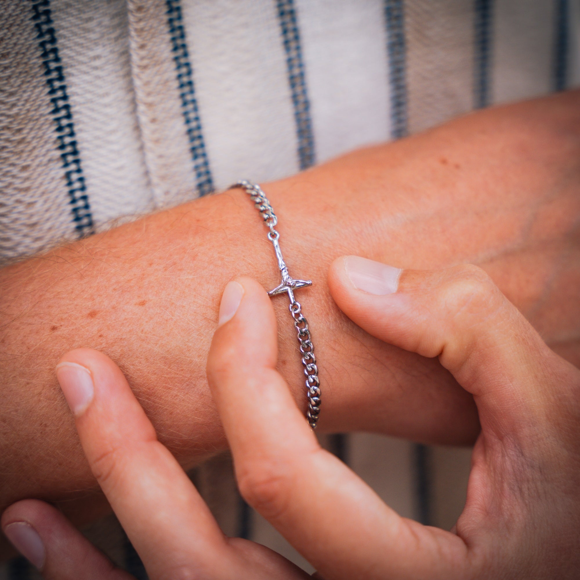 Close-up of a person wearing a silver bracelet with a cross charm on a striped fabric background.