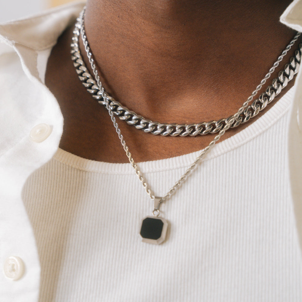 Person wearing two silver chain necklaces with a black pendant on a white shirt.