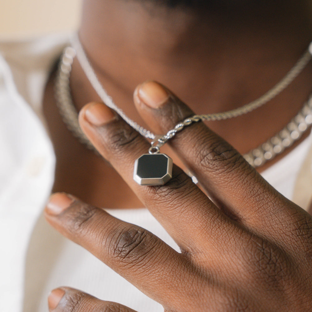 Close-up of a hand wearing a silver ring with a hexagonal pendant on a neutral background
