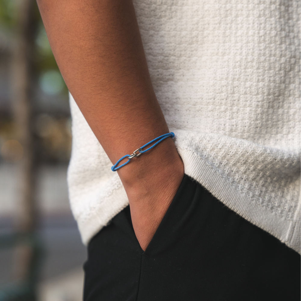 A person wearing a blue and gold bracelet on their wrist, with a white sweater and black shorts.