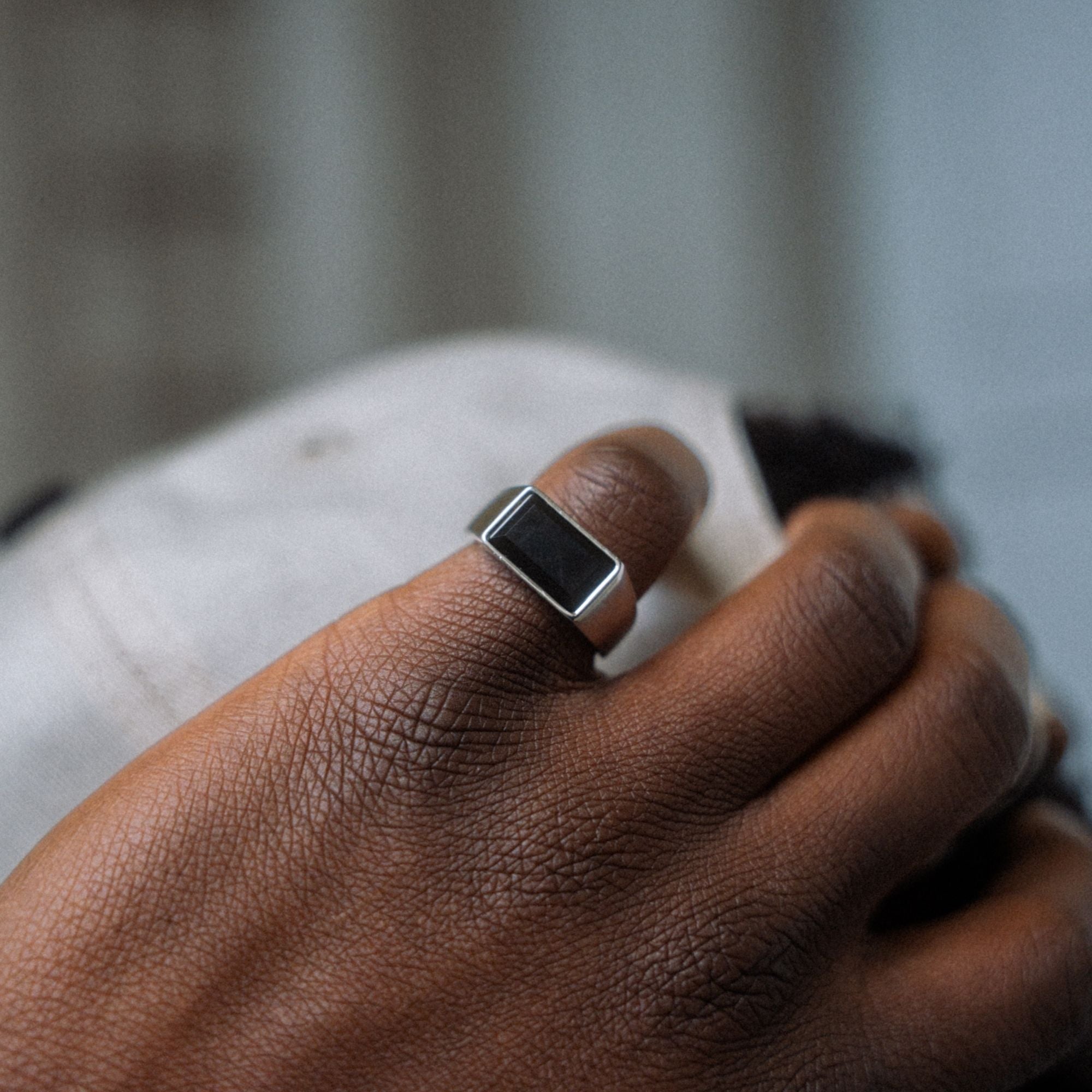 A silver-toned signet ring with a black rectangular face, worn on a person's finger.