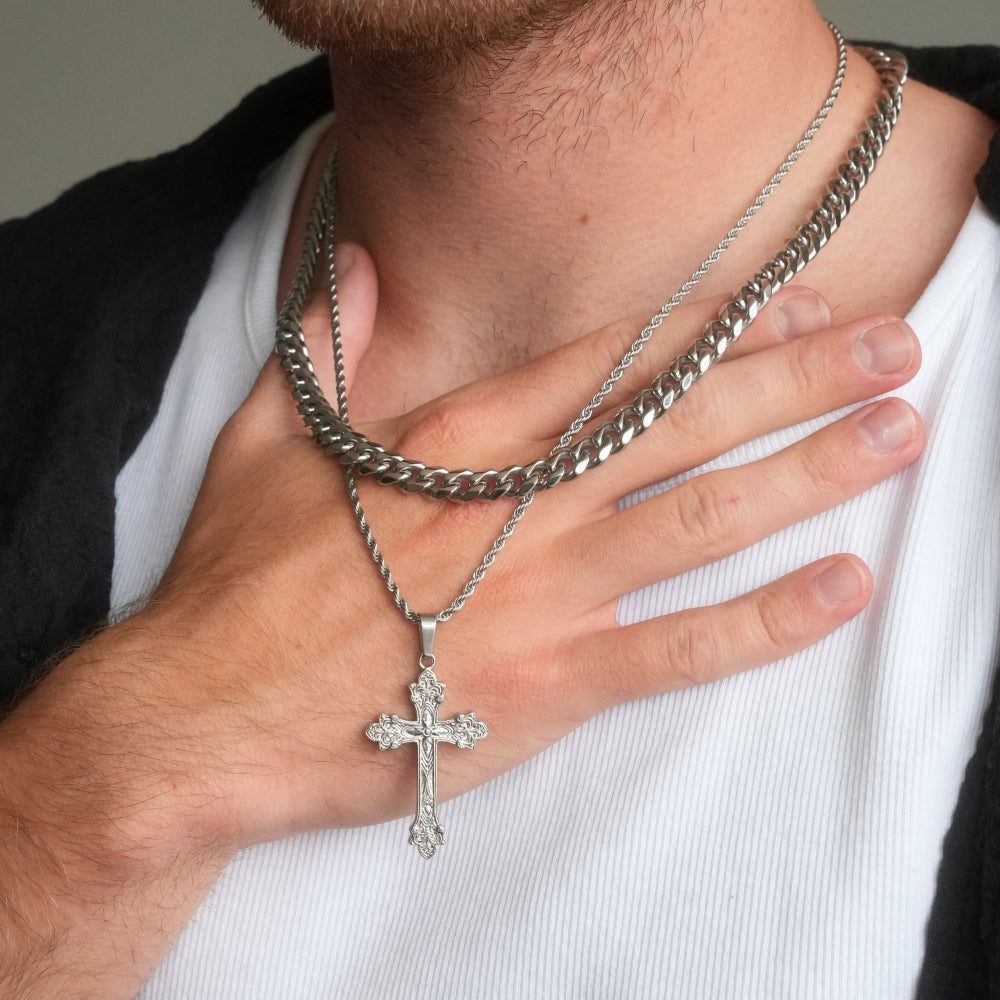 Silver chain necklace with a cross pendant worn by a person on a plain background