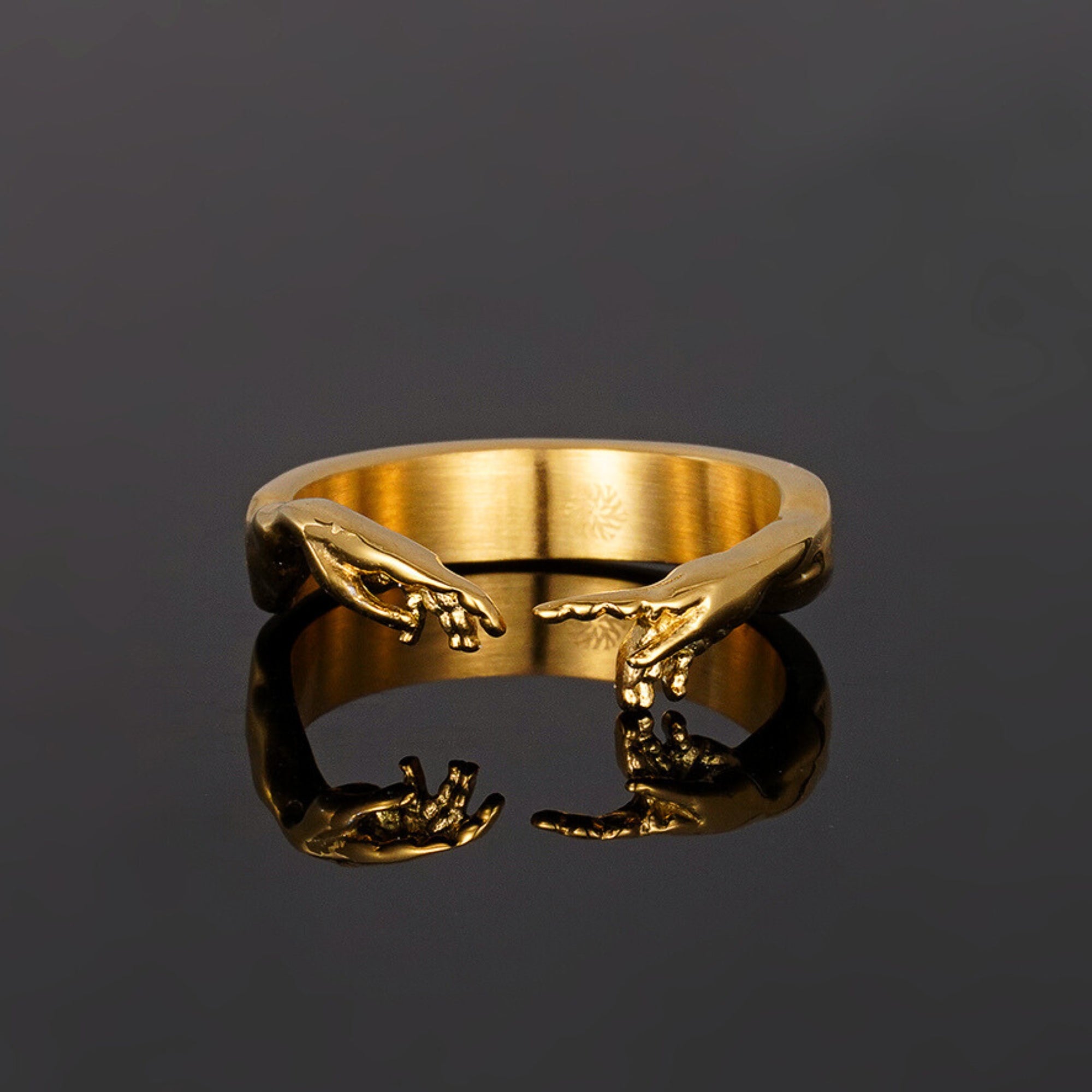 Gold ring with hand designs on a dark background