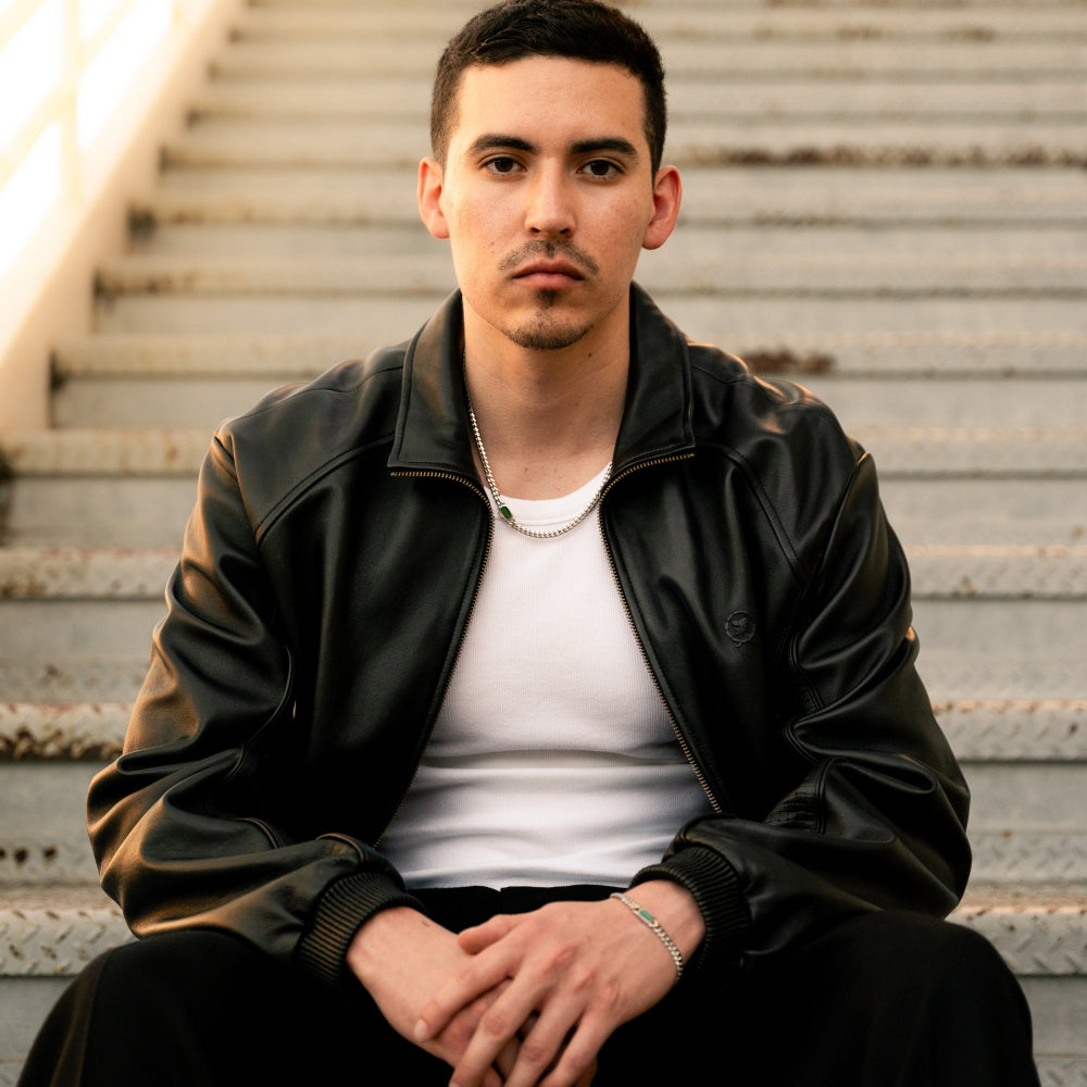 Man wearing a black leather jacket sitting on metal stairs.