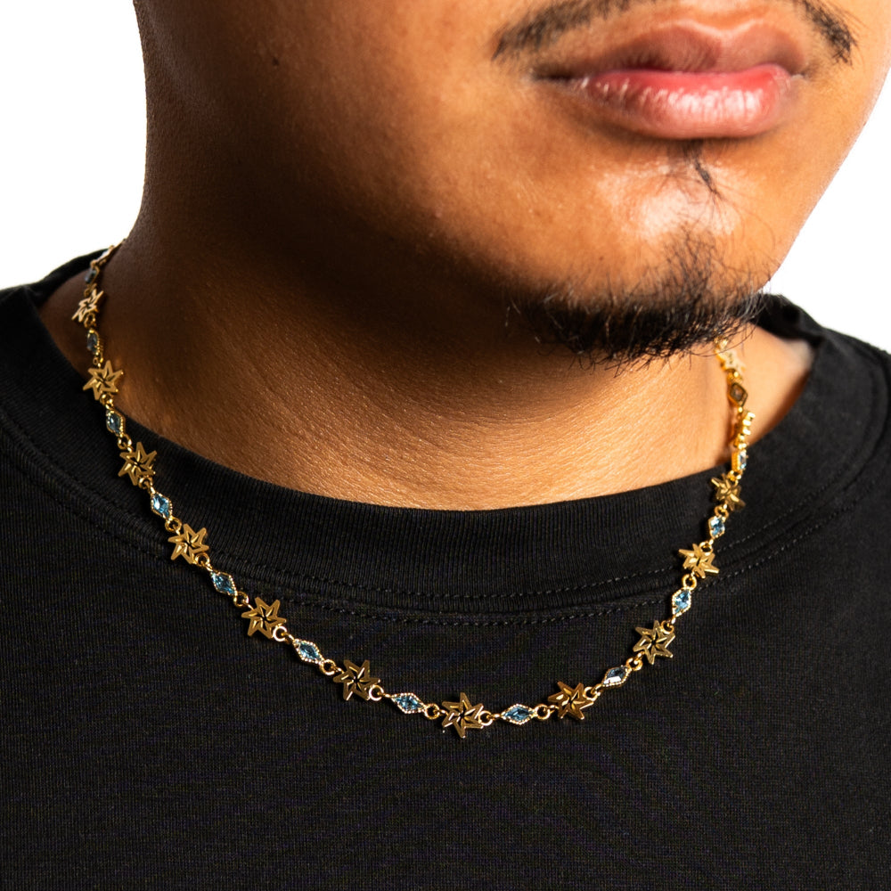 Man wearing a gold necklace with star-shaped links on a plain background