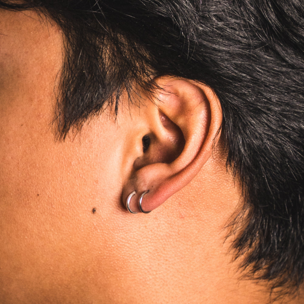 Close-up of an ear with a hoop earring, surrounded by dark hair.