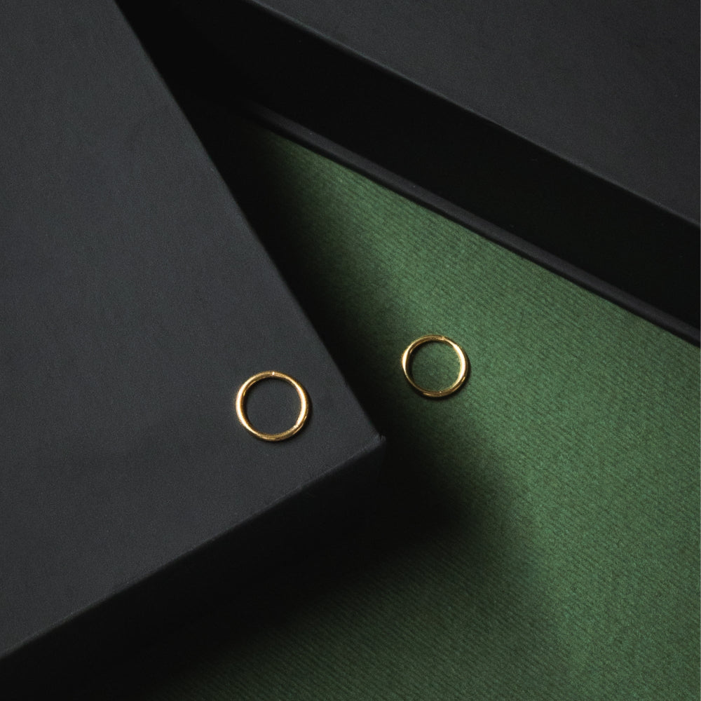 Two gold hoop earrings on a dark green surface with a black background
