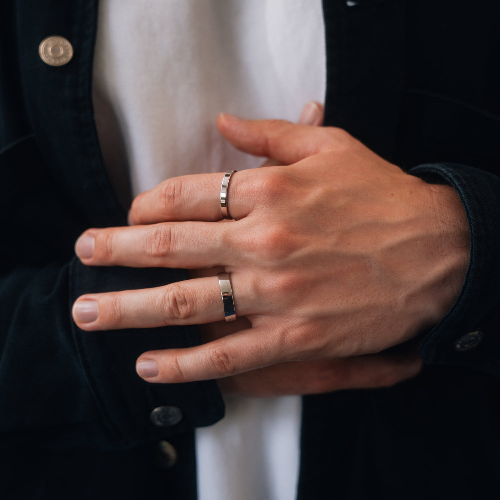 Close-up of a person's hands with two rings on fingers, wearing a dark jacket.
