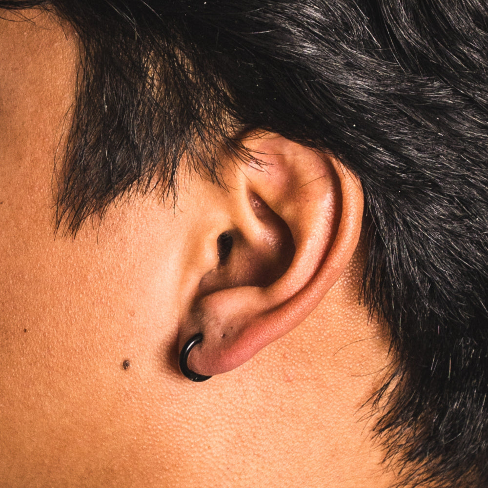 Close-up of an ear with a black earring on a person with dark hair.
