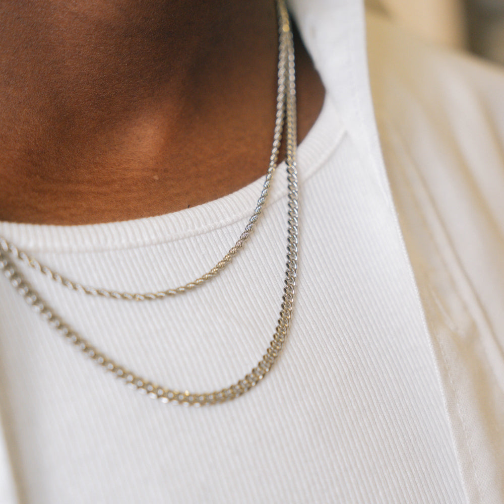 Close-up of a person wearing two gold necklaces on a plain background