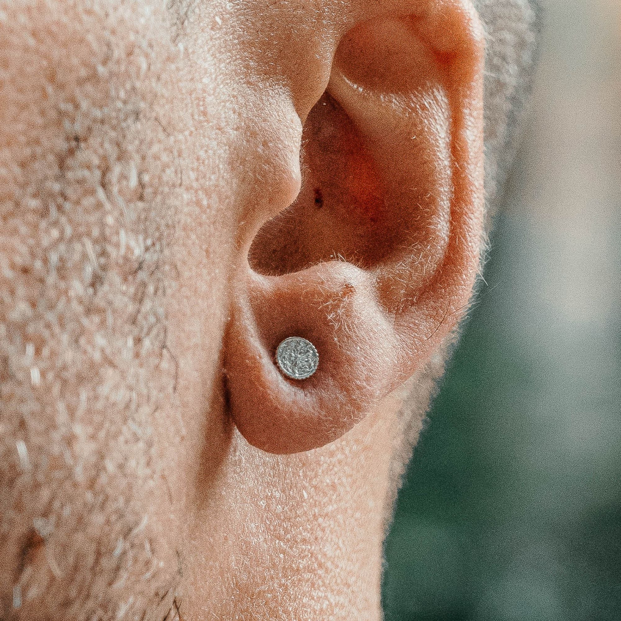 A close-up of a person's ear wearing a small, round, silver-toned stud earring.