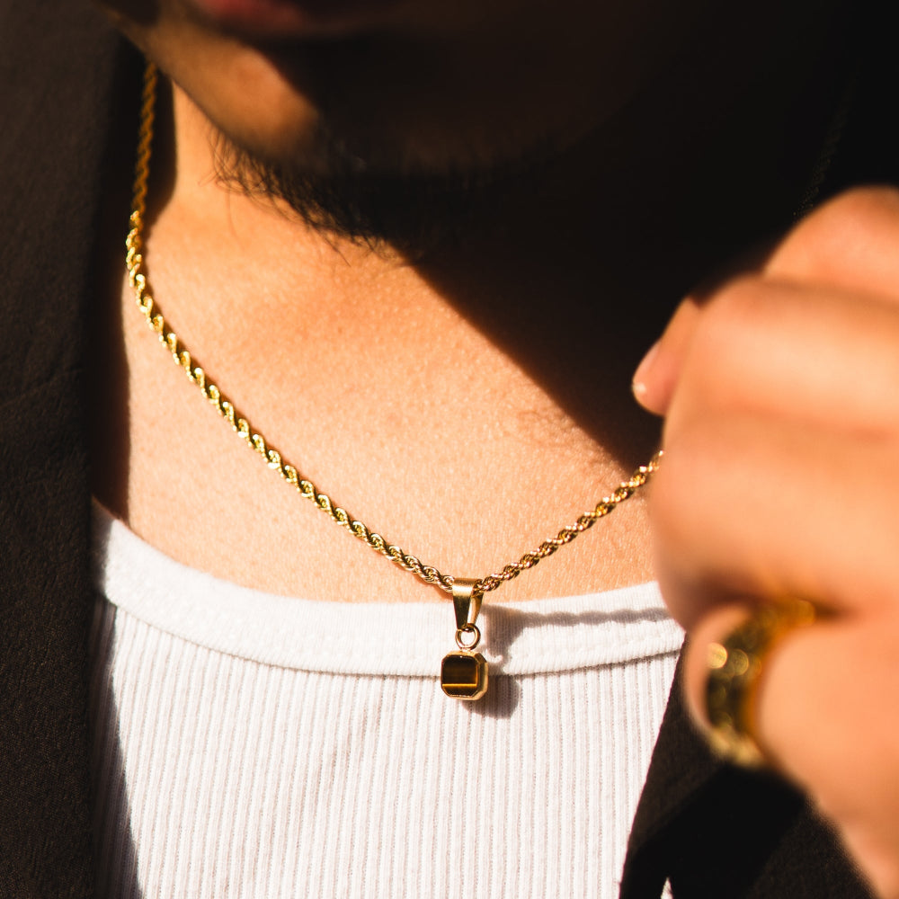 Close-up of a person wearing a gold necklace with a pendant, holding a glass.