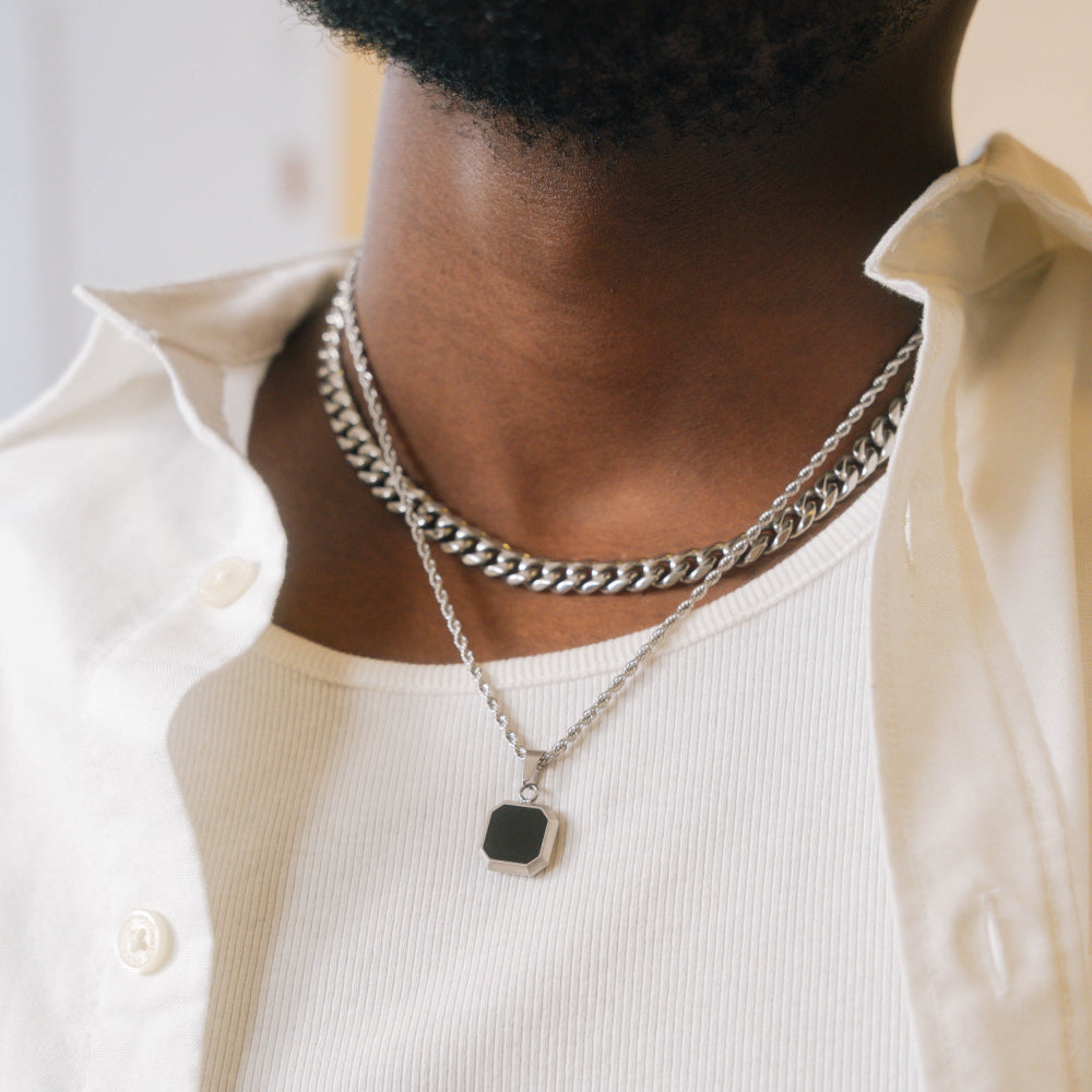 Person wearing a silver chain necklace with a pendant on a plain background