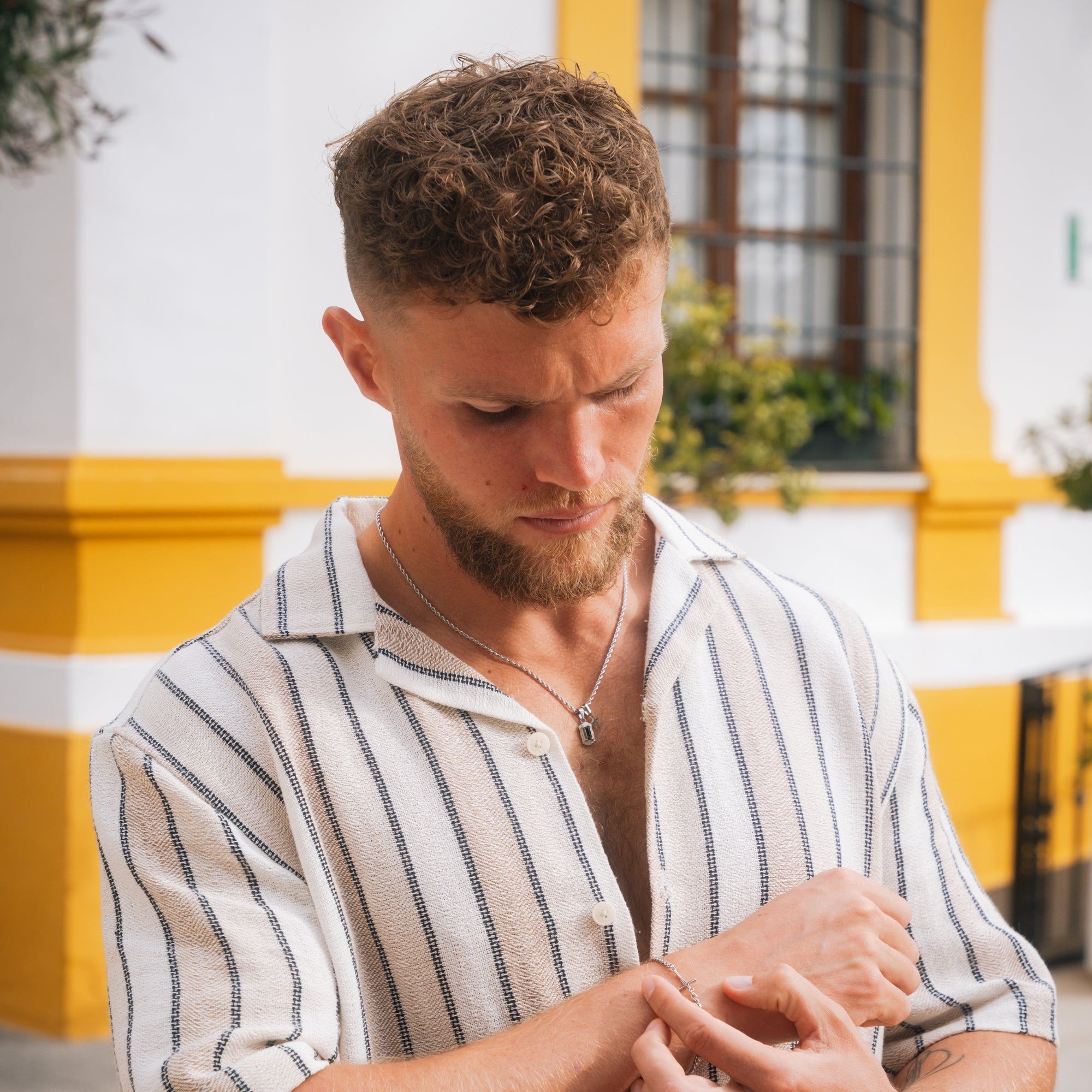 Man wearing a striped shirt looking at his watch with a yellow building in the background