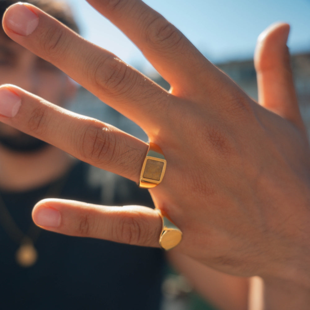 Hand wearing a gold ring with a blurred background