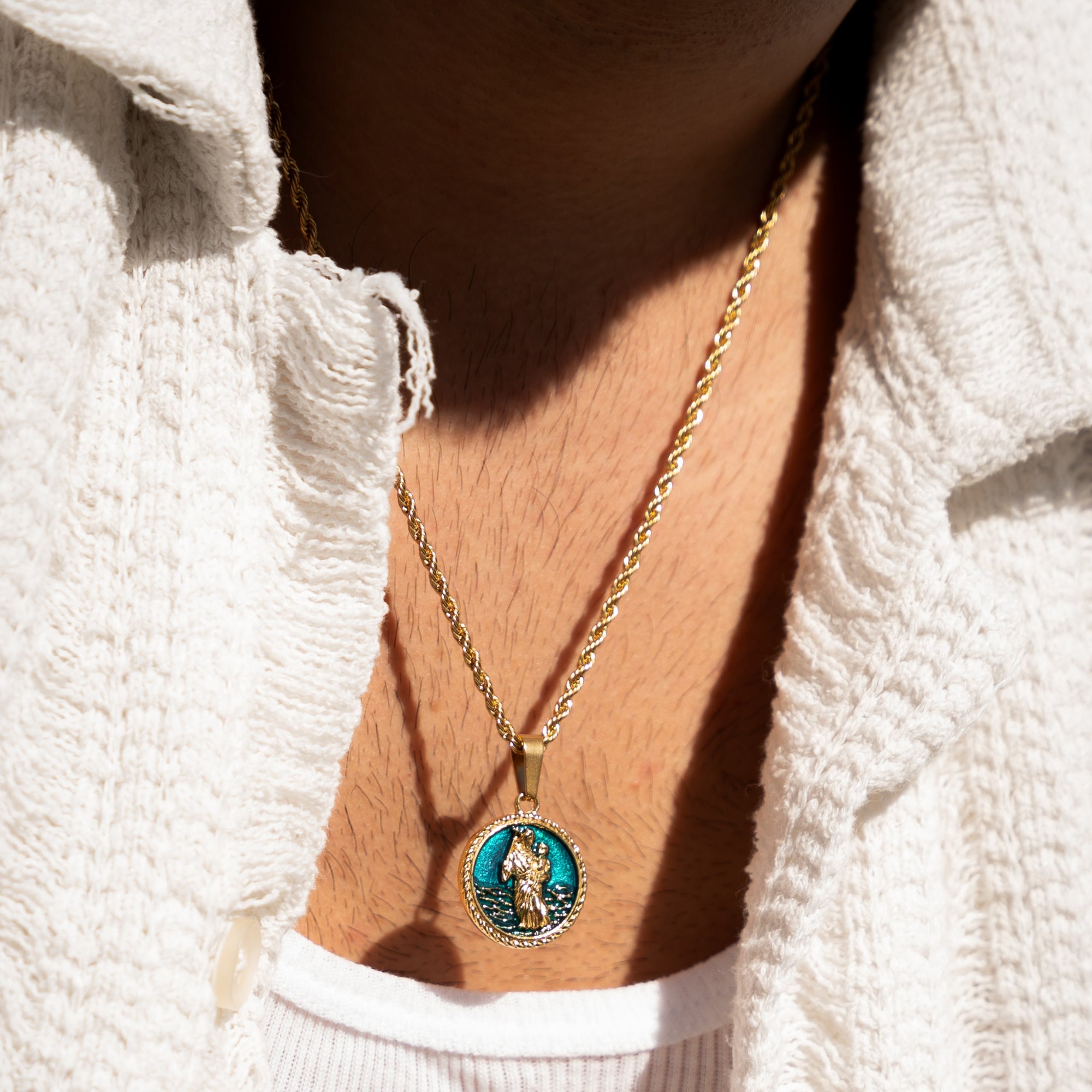Gold necklace with a pendant worn by a person in a white textured garment.