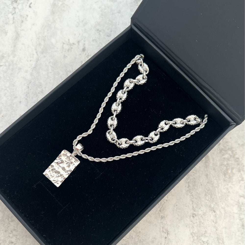Silver necklace with a rectangular pendant in a black jewelry box on a light gray surface